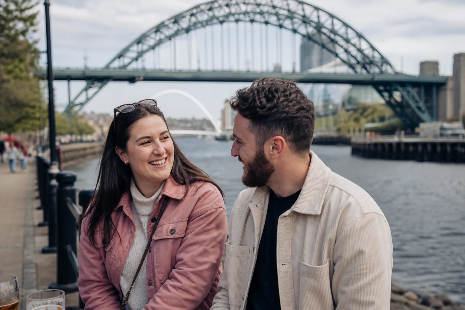 Two people talking beside the River Tyne with Newcastle and Gateshead in the background